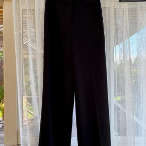 Svarta wide byxor från H&M - Säljer ett par svarta byxor från H&M i storlek 40. De har en bred och rak passform med hög midja och är tillverkade i ett skönt materiel. Perfekta för en chill och stilren look, med knappstängning i midjan.