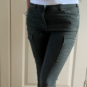 Gröna cargopants från Dr Denim - Snygga mörkgröna cargopants från Dr Denim i modellen Dezie. Byxorna har låg midja, stora fickor på sidorna och dragkedjor vid bensluten. Tillverkade i mjukt bomullsmaterial med en slim passform. Perfekta för en chill och trendig look.