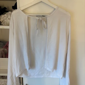 Vit långärmad topp med knyt - Vit långärmad topp från Est. 1999 med rund halsringning och snygg knytning framtill. Enkel och stilren design som passar perfekt till jeans eller kjol. Mjuk och skön i bomullsmaterial.