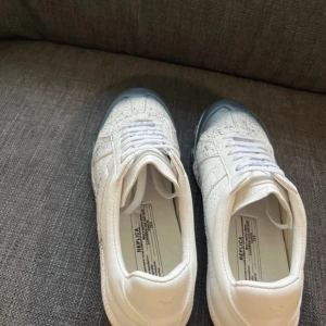 MM gats sneakers vit/blå - MM gats sneakers i vitt skinn med blå tå och blått stänkmönster. Klassisk låg modell med snörning och rund tå. Snygg och unik design som sticker ut, perfekt för dig som gillar statement sneakers. Box och extra snören medkommer till skorna+kvitto från NK.