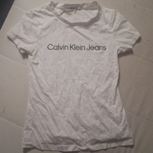 Vit Calvin Klein Jeans t-shirt - Helt oanvänd. Vit t-shirt från Calvin Klein Jeans i klassisk modell med rund hals och korta ärmar. Nypris runt 350 mitt pris 250 Stor logga tryckt framtill i svart. Tillverkad i mjuk bomull som känns skön mot huden. Perfekt för en clean och stilren look.
