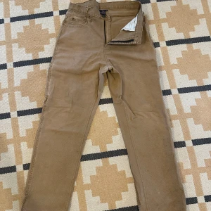 Bruna arbetsbyxor Beyond Retro/ dickies 32 - Snygga bruna arbetsbyxor från Beyond Retro/ dickies i storlek 32. Klassisk rak passform. Byxorna har en vintagekänsla och är perfekta för dig som gillar retrostil i arbetsformat.