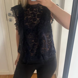 Mörkblå spetsblus från Zara - Supersnygg mörkblå blus från Zara i transparent spets med blommigt mönster. Blusen har ärmlös design med volangkant vid axlarna och rund hals. Använd fåtal gånger! Inga defekter