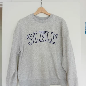 Grå sweatshirt  Gina Tricot M - Säljer en grå sweatshirt från Gina Tricot i storlek M. Tröjan har SCFLH broderat i blått på bröstet, rund hals och ribbade muddar vid ärmslut och nederkant. Perfekt för chill dagar och enkel att matcha med jeans eller mjukisbyxor.