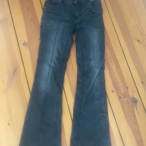 Svarta bootcut jeans med fickor på sidorna - Snygga svarta jeans från Lindex med bootcut-modell och markerade sömmar längs benen. Byxorna har stora fickor framtill och stängs med två knappar och dragkedja. Perfekta för dig som gillar en retroinspirerad look.