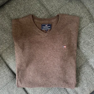 Brun v-ringad tröja från Lexington - Brun v-ringad tröja från Lexington med liten broderad logga på bröstet. Tröjan är i mjuk ullblandning, har långa ärmar och ribbade muddar. Perfekt för lager-på-lager och chill höst- eller vinterstil.