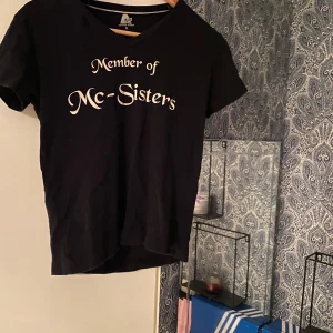 Svart t-shirt Member of Mc-Sisters - Svart t-shirt från Active Wear med vit text 'Member of Mc-Sisters' på bröstet. Klassisk v-ringning och korta ärmar. Perfekt för dig som vill sticka ut med en cool statement-tee. Skön passform och mjukt material.