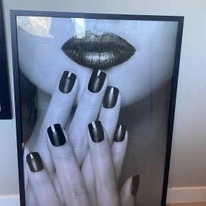 Tavla  - Det här är en stor, stilren poster med ett svartvitt motiv av läppar och händer med mörkt nagellack. Perfekt för dig som gillar mode, skönhet och vill ha en modern touch i ditt rum. Passar utmärkt som dekoration för unga vuxna och tonåringar som vill uttrycka sin personliga stil.