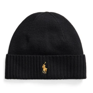 Polo Ralph Lauren mössa i svart - Svart ribbstickad mössa från Polo Ralph Lauren med klassisk gul broderad logga framtill. Enkel och stilren design med uppvikt kant som ger extra värme. Perfekt accessoar för kyliga dagar och snygg till streetwear.