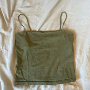 Olivgrön linnetopp från Gina Tricot - Snygg olivgrön linnetopp från Gina Tricot med tunna axelband och enkel, rak passform. Perfekt att styla med jeans eller kjol för en chill look. Tillverkad i mjuk bomull som känns skön mot huden.