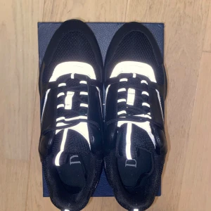 Svarta sneakers med reflexdetaljer - Chunky svarta sneakers med reflekterande detaljer och meshpaneler. Skorna har snörning, robust sula och coola vita reflexlinjer som syns i mörker. Kombination av skinn och textil ger en lyxig och sportig vibe. Perfekta för dig som vill sticka ut.