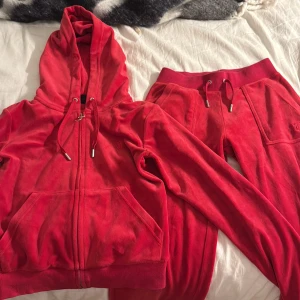 Röda mjukisbyxor i velour - Säljer ett par röda mjukisbyxor i mjuk velour med bred resår i midjan och snörning. Byxorna har fickor fram och bak med lock och tryckknappar, samt raka ben. Perfekta för chill dagar och riktigt skön passform.