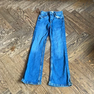 Blå jeans med slits från MNG - Snygga blå jeans från MNG med raka ben och cool slits nertill. Klassisk femficksmodell i jeansmaterial med kontrastsömmar. Perfekta för dig som gillar en avslappnad och trendig look.