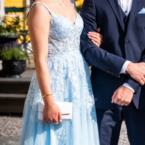 Ljusblå balklänning med spetsdetaljer - Säljer en drömmig ljusblå långklänning med tunna axelband och v-ringad urringning. Klänningen har transparent mesh upptill med broderade blommor och ett flytande, svepande kjolparti i flera lager. Perfekt för bal! Använd vid 1 tillfälle 🥰nypris 2800