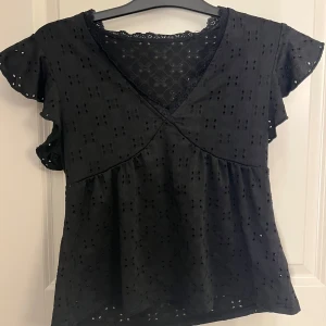 Svart blus med spets och volangärm - Svart blus med v-ringning, spetsdetaljer vid halsen och korta volangärmar. 