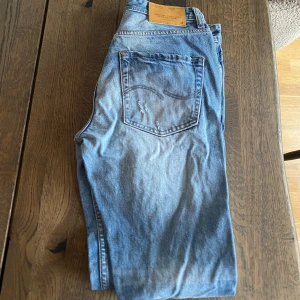 Blå slitna jeans från Jack and Jones  - Säljer ett par blå jeans från Jack and Jones  med snygga slitningar och klassisk femficksdesign. Jeansen har rak passform och normal midja. Perfekt för dig som gillar en avslappnad och cool stil.