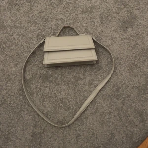 Grå  axelväska från Gina Tricot - Snygg beige axelväska från Gina Tricot med stilren, fyrkantig form och lock. Väskan har både handtag och lång axelrem, perfekt för att bära på olika sätt. Tillverkad i slätt syntetmaterial och har ett innerfack med dragkedja. Pris kan diskuteras vid snabb affär!💗