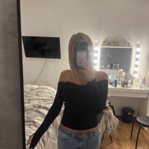 Svart offshoulder topp från Gina Tricot - Säljer en svart, tight offshoulder topp från Gina Tricot. Toppen har långa ärmar och en croppad passform som sitter snyggt över axlarna. Perfekt att styla med jeans eller kjol för en trendig look.