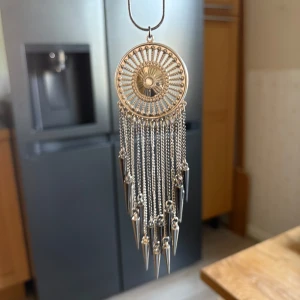 Silvrigt halsband med kedjor och spikes - Unikt halsband i silverfärgad metall med rund, solinspirerad medaljong och långa kedjor med coola spikformade hängen. Kedjan är tunn och smidig, och hela smycket ger en edgy och boho vibe. Perfekt för dig som vill sticka ut med detaljer som verkligen syns.