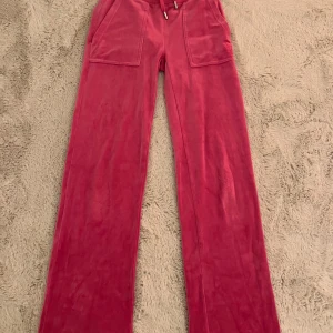 Rosa mjukisbyxor från Juicy Couture XXS - Snygga rosa mjukisbyxor från Juicy Couture i storlek XXS. Byxorna har breda ben, stora fickor fram och bak samt snören i midjan. Tillverkade i mjuk och stretchig polyesterblandning för maximal komfort. Perfekta för en chill och trendig look.