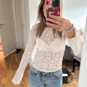 Vit spetsblus med långa ärmar - Säljer en superfin vit blus i spets med långärmad design och rund halsringning. Blusen är genombruten och har ett feminint mönster i spetsmaterial. Perfekt att styla med jeans eller kjol för en trendig look.
