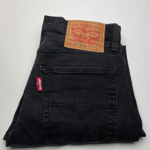 Levi's 512 svarta jeans  - Svarta Levi's 512 jeans med klassisk röd Levi's-tag på bakfickan och ikonisk patch bak i midjan. Jeansen har en smal passform och är tillverkade i mjukt denimtyg. Perfekta för dig som gillar en clean och tidlös look.