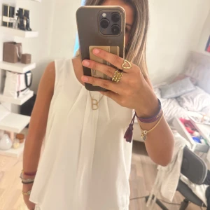 Vit blus med spetskant från KISSER - Superfin vit blus i luftig polyester med spetsdetalj längst ner. Ärmlös modell med snygg öppning i ryggen och veck framtill. Perfekt till jeans eller kjol för en fräsch look. Enkel att matcha och riktigt söt detalj med spetsen.