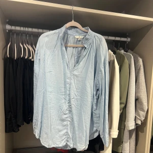 Ljusblå blus/skjorta - Säljer en ljusblå tunn blus/skjorta i avslappnad passform. Har en mjuk, rynkad krage och v-ringning utan knappar framtill. Behöver bara en omgång med strykjärnet 😄