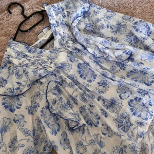 Blåvit blommig blus från Zara - Supersöt blåvit blus från Zara med blommigt mönster och volangdetaljer. Lätt och luftig i bomull, perfekt för varma dagar. Blusen har fina veck och romantiska detaljer längs halsringningen. Helt ny och oanvänd, har ingen tecken på användning har endast testat den😇 nypris: 470kr