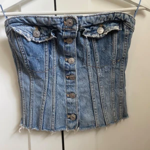 Jeans tubtopp med knappar från Zara - Jeans tubtopp från Zara med knappar framtill och smockad baksida. Perfekt till jeans eller kostymbyxor. Strl: xs