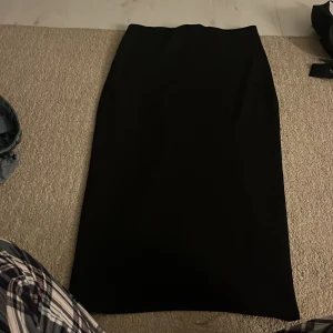 Svart långkjol från 157 - En stilren svart långkjol från 157 i storlek S. Kjolen har en rak och enkel design som gör den lätt att matcha med olika toppar. Perfekt för dig som gillar minimalistisk stil och vill ha en klassisk bas i garderoben.