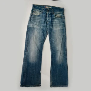 Vintage Levi's 512 bootcut jeans med slitningar - Säljer dessa vintage Levis 512 bootcut jeans. Extremt snygga med mycket karaktär. Råa kanter vid benslut, fades vid knävecken, slitningar vid fickorna, etc. Har dock lite fläckar på baksidan, en konsekvens av regelbunden användning. De är egentligen 32W/34L i storleken men är uppsydda till en 32 i längd. Midja (tvärs över): 41,5 cm. Ytterbenslängd: 99,5 cm. Benöppning: 23 cm.