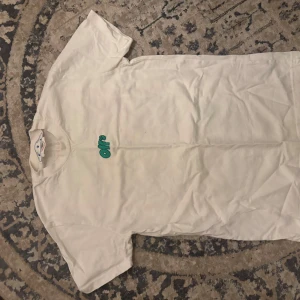 Off-White t-shirt med grafiskt tryck - Vit t-shirt från Off-White med coolt grafiskt tryck på ryggen i grönt, rosa och svart. Framsidan har en liten Off-White-logga i grönt. Klassisk passform med rund hals och korta ärmar. Perfekt för dig som gillar streetwear och unika prints.