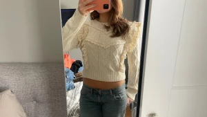 Stickad volangtröja från Mango - Supersöt stickad tröja från Mango i ljus beige med volangdetaljer och spets längs axlar och bröst. Tröjan har ett snyggt kabelstickat mönster, croppad passform och långa ärmar. Perfekt för dig som gillar romantisk och trendig stil. Står storlek L men sitter mer som en S