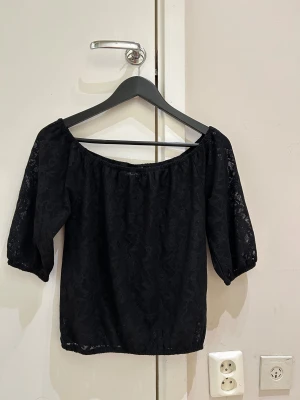 Ny Svart spetsblus från Nelly XS - Säljer en svart blus från Nelly i storlek XS. Blusen har offshoulder-modell med halv-långa ärmar och är gjord i ett genombrutet spetsmaterial med blommigt mönster. Perfekt för dig som gillar romantisk och trendig stil.