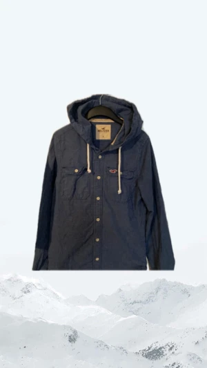 Hollister overshirt  - Blå overshirt  från Hollister med huva och vita snören. Skjortan har två bröstfickor med knappar och Hollister-logga broderad på ena fickan. Långärmad och tillverkad i bomull, perfekt för en avslappnad stil.