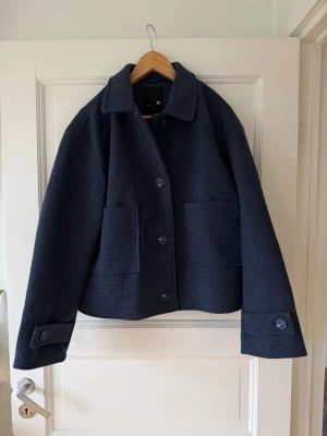 Mörkblå jacka - Aldrig använd  - Snygg mörkblå jacka från Lager 157. Jackan har en boxig passform, stora framfickor och stängs med  Klassisk krage och detaljer vid ärmslut. Perfekt för höst och vinter. Ny med prislapp! 