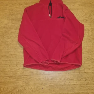 Röd fleece-tröja med half zip - Röd fleece-tröja med half zip och liten ficka med dragkedja på bröstet. Perfekt för kyliga dagar och enkel att dra på över en t-shirt. Långärmad och mjuk, med avslappnad passform och hög krage.