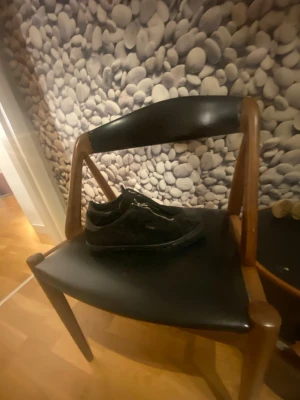 Svarta mocka sneakers från ARIGATO - Snygga svarta sneakers från ARIGATO i mjuk mocka med silverfärgad dragkedja framtill istället för klassisk snörning. Låg modell med platt sula och diskret guldfärgad logga på sidan. Perfekt för dig som gillar stilrena och moderna detaljer.