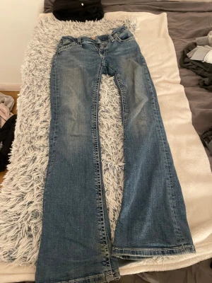 Blå bootcut jeans med broderade fickor - Snygga blå jeans med bootcut passform, lite slitna vid bensluten. Baksidan har två fickor med vit broderad kant och dekorativa knappar. Jeansen har klassisk femficksdesign och är tillverkade i jeansmaterial med en tvättad look. Säljer pga att de är lite för korta för mig, de är i strl 158. Pris kan diskuteras och kan skicka fler bilder ifall att det önskas🥰