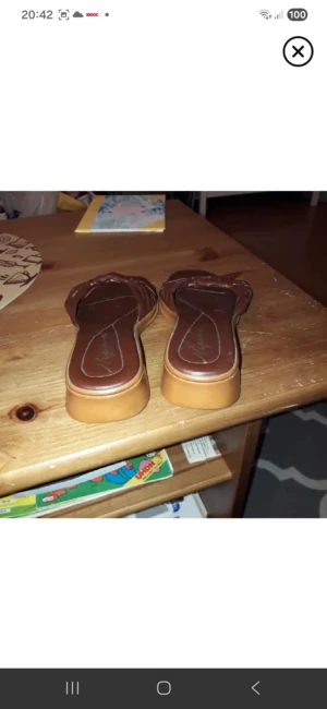 Bruna sandaler med flätad detalj - Snygga bruna sandaler från Mojama med flätad detalj över foten och platt sula. Skorna har fyrkantig tå och är tillverkade i syntetmaterial med en beige sula. Perfekta för sommarens alla tillfällen.