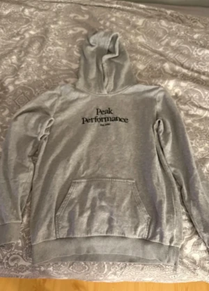 Grå hoodie Peak Performance 170 - Snygg grå hoodie från Peak Performance med svart logotyp på bröstet. Tröjan är använd men k bra skick ändå 