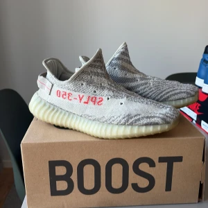 Adidas Yeezy Boost 350 V2 Blue Tint Storlek EU42/US 8.5 - Säljer ett par Adidas Yeezy Boost 350 V2 Zebra med grått och vitt stickat mönster, röd SPLY-350 text på sidan och genomskinlig, ribbad sula. Skorna har en låg profil och är tillverkade i syntetmaterial och textil för en skön och flexibel känsla. VÄLDIGT SKÖNA SKOR 😁 SÄLJER PGA FÖR SMÅ