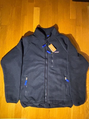 Patagonia Jacka - Säljer en helt oanvänd Patagonia-jacka i storlek L, färg blå – tags kvar. Köpt i fel storlek (jag är 174 cm på bilden), så den har aldrig kommit till användning. Jackan har perfekt passform och kvalitet som Patagonia är känt för: lätt, slitstark och riktigt snygg.