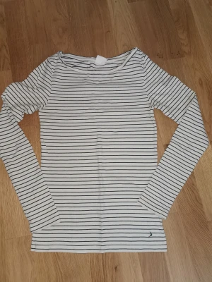 Jättefin långärmad randig tröja Vit/svart från Boomerang, storlek XS - Vit långärmad tröja med svarta horisontella ränder och en liten broderad Boomerang logga längst ner. Köpt på Boomerang butiken. Tröjan har en rundad hals och är gjord i mjuk bomull. Passformen är normal och den är enkel att matcha med jeans eller kjol. Den är i fint använt skick. Storlek XS