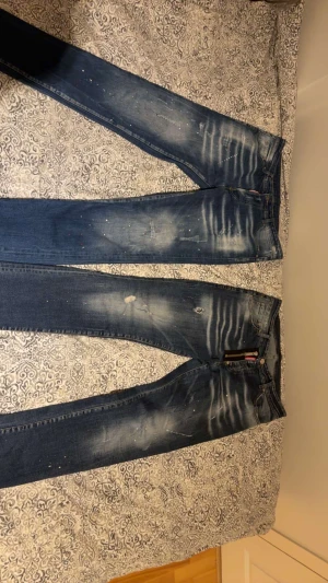 Replay jeans i blått med slitningar - Två par blå Replay jeans med slitna detaljer, ljusa partier och färgstänk. Klassisk femficksmodell med raka ben och låg midja. Jeansen har tydliga slitningar och tvättade effekter för en cool, använd look. Perfekta för dig som gillar streetstyle.