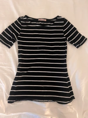 Svartvit randig topp från Anna Field - Svart topp med vita horisontella ränder från Anna Field. Modellen har rund halsringning och korta ärmar. Toppens passform är normal och materialet känns mjukt och stretchigt, troligen bomull eller bomullsblandning. Perfekt för en stilren och enkel look.