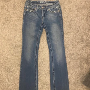 Blå jeans med broderade bakfickor - Snygga blå bootcut jeans från ViViDiva med broderade detaljer och nitar på bakfickorna. Klassisk femficksmodell med raka ben och låg midja. Jeansen har ljus tvätt och dekorativa sömmar, perfekt för dig som gillar statement-jeans. Midja rakt över: 33cm Lår: 21cm Innerben: 82cm 