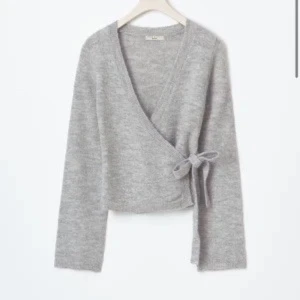 Stickad tröja  - Supermysig grå omlottkofta från Gina Tricot med v-ringning och knyt i sidan. Koftan är stickad och har långa ärmar, perfekt för lager-på-lager. Enkel att matcha med jeans eller kjol för en chill look.