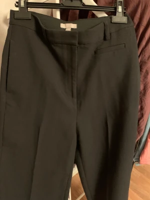 Svarta kostymbyxor med raka ben - Snygga svarta kostymbyxor med raka ben och klassisk passform. Byxorna har hällor för bälte, diskreta fickor fram och bak med knappdetaljer. Perfekta för en clean och stilren look. Materialet känns mjukt och följsamt.